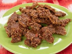 a green plate topped with beef pieces on top of a red and white table cloth