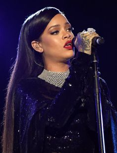 a woman with long black hair and piercings on her head singing into a microphone