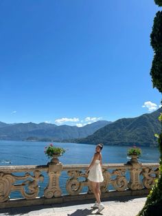 a woman in a white dress is standing on a balcony overlooking the water and mountains