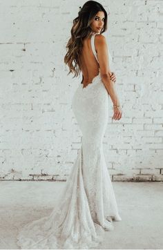 a woman in a white dress is standing near a brick wall and looking back at the camera