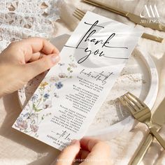 a person holding a thank card on top of a plate with gold forks and knives