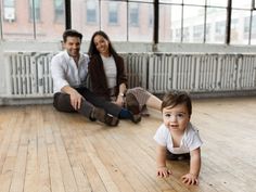 a baby crawls on the floor while his parents sit behind him in an empty room