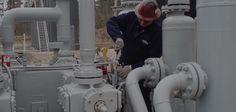 a man is working on pipes in an oil and gas plant with other equipment behind him