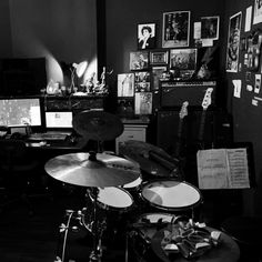 black and white photograph of a drum set in front of a computer desk with many pictures on the wall