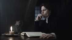 a man sitting at a table in front of a book with a candle on it