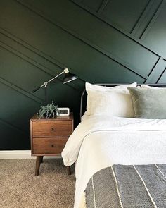 a bedroom with dark green walls and white linens on the bed, along with a wooden night stand