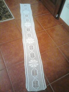 a white crocheted table runner on the floor in a room with tile floors