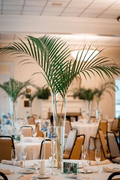 there is a tall vase with palm leaves in it on the table set for an event