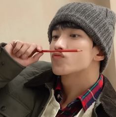 a young man wearing a hat and holding a pencil in his mouth