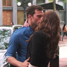 a man kissing a woman on the cheek while standing in front of a parked car