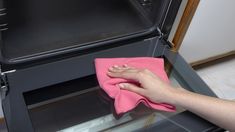 a person cleaning an oven with a pink microfit towel and a hand on top of it