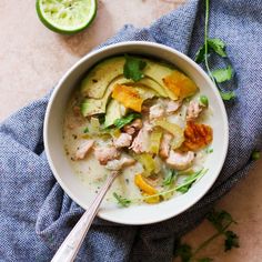 a white bowl filled with chicken and vegetable soup next to limes on a blue towel