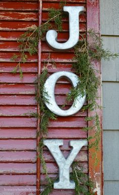 the word joy is spelled in white letters on an old red door with greenery