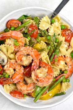 a white bowl filled with pasta, shrimp and asparagus on top of a table