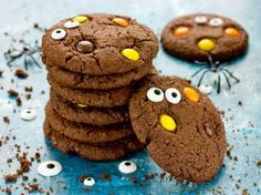 chocolate cookies with eyes and googly eyes are on a blue surface next to sprinkles