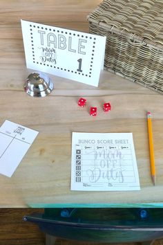 a wooden table topped with red dices next to a basket and two paper signs