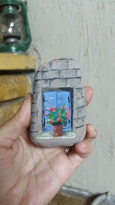 a hand holding a small brick window with potted flowers