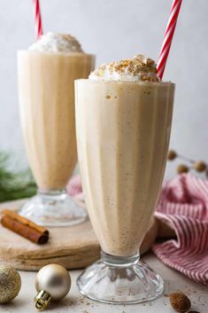 two glasses filled with milkshakes on top of a wooden board next to christmas decorations