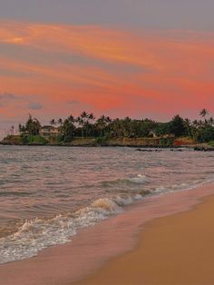 a beach with waves coming in to the shore and palm trees on an island in the distance