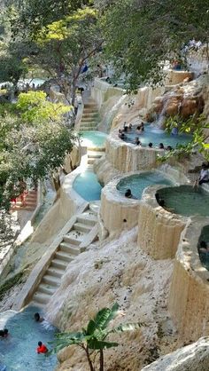 people are swimming in an artificial pool surrounded by rocks and trees, with stairs leading up to the water