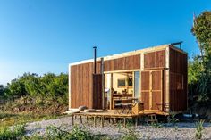 a small wooden house sitting on top of a gravel field next to trees and bushes