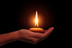 a person holding a lit candle in their hand on a dark background with space for text