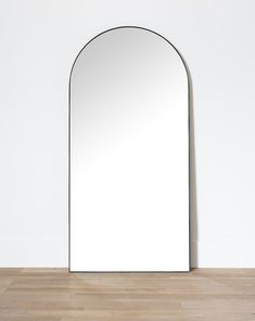 an arched mirror on the floor in front of a white wall and wood flooring