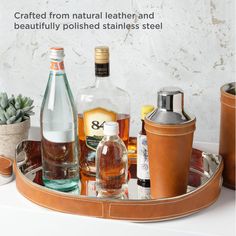 an assortment of alcohol bottles and glasses on a tray with the words, crafted from natural leather and beautifully polished stainless steel