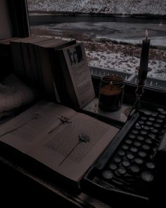 an open book sitting on top of a desk next to a candle and some books