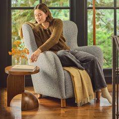 a woman sitting in a chair with a book on her lap looking out the window