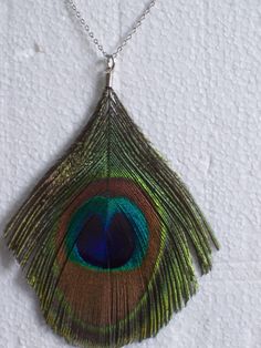 a peacock feather pendant hangs from a chain on a white surface with small holes in it