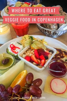 a white plate topped with lots of food next to fruit and cheese on top of a wooden table