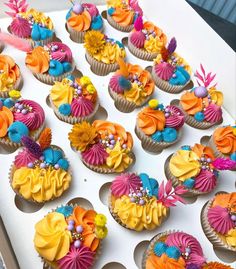 cupcakes decorated with colorful icing and flowers on a white tableclothed surface