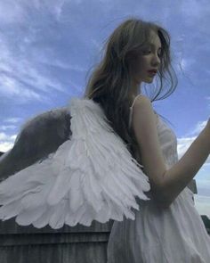 a woman dressed in white holding a cell phone with angel wings on her shoulders and arms