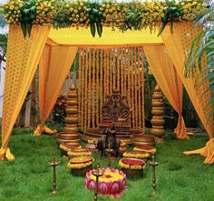 an outdoor wedding setup with yellow draping and flowers on the grass, surrounded by other decorations