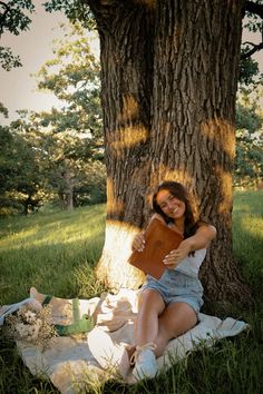 a woman sitting under a tree holding a book