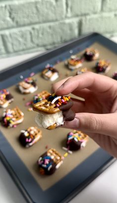 a person is holding up some food on a cookie sheet with icing and sprinkles