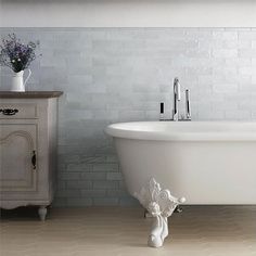 a white bath tub sitting next to a wooden cabinet with flowers on top of it