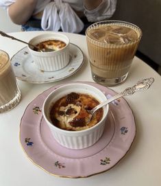 there is a bowl of soup on the table with two cups and spoons next to it