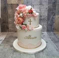 a white cake with pink flowers and a cross on the top that says alesia