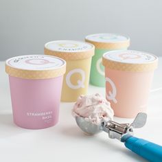 three ice cream cups with spoons next to them on a white surface, one has pink frosting and the other is blue