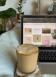 a laptop computer sitting on top of a bed next to a cup filled with liquid