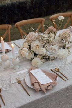 the table is set with white flowers and gold cutlery, napkins, silverware, and candles