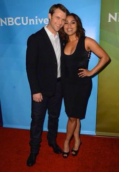 a man and woman standing next to each other in front of a nbc logo on a red carpet