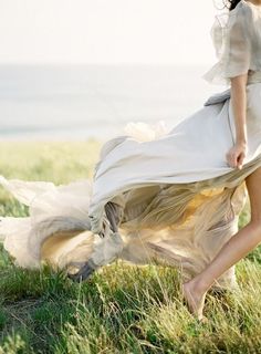 a woman is walking in the grass with her dress flowing over her body and shoes on