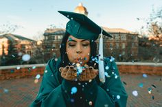 a woman wearing a green graduation gown blowing confetti in front of her face