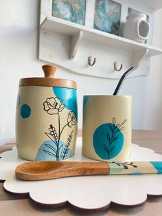 two mugs with flowers painted on them are next to a wooden spoon and toothbrush holder