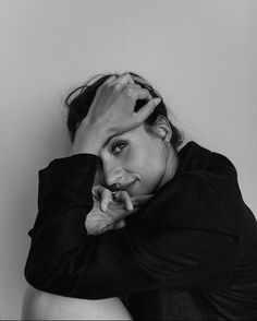 a black and white photo of a woman with her hands on her head, leaning against the wall