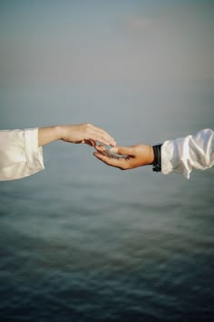 two people holding each other's hand over the ocean with water in the background