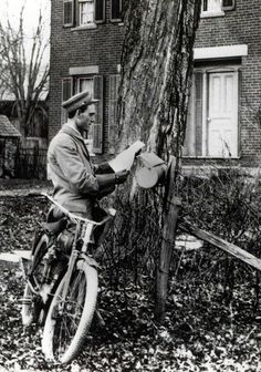 an old photo of a man sitting on a bike next to a tree in front of a house